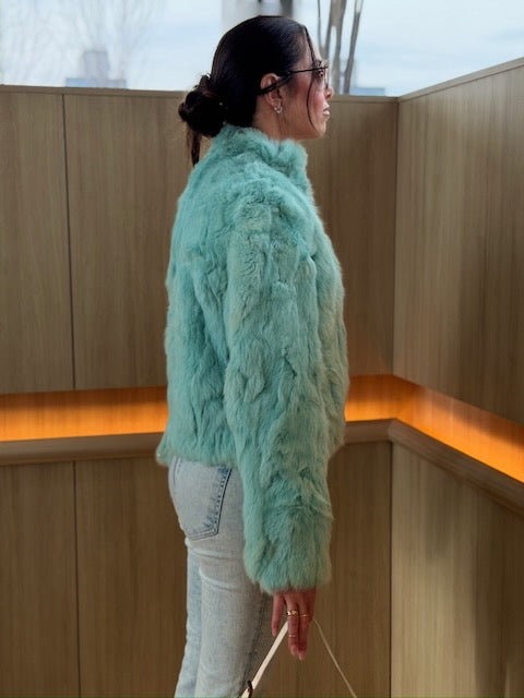 Person wearing a light blue fur coat standing indoors with wooden panels and warm lighting.