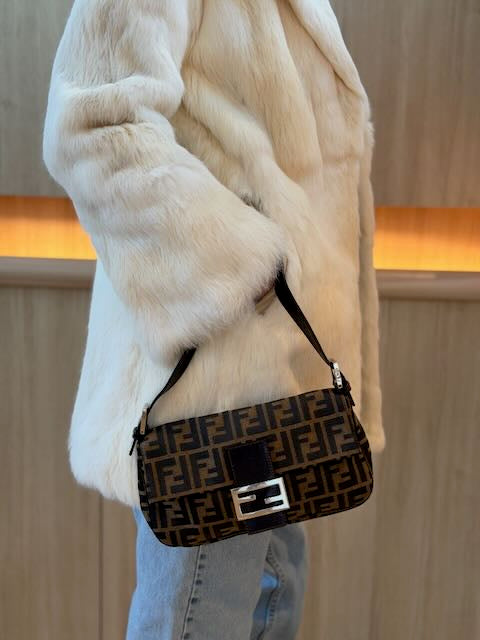 Person wearing a white fur coat holding a patterned handbag.
