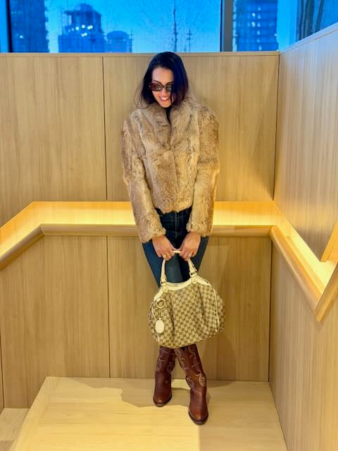 Woman standing in a wooden booth holding a patterned handbag.
