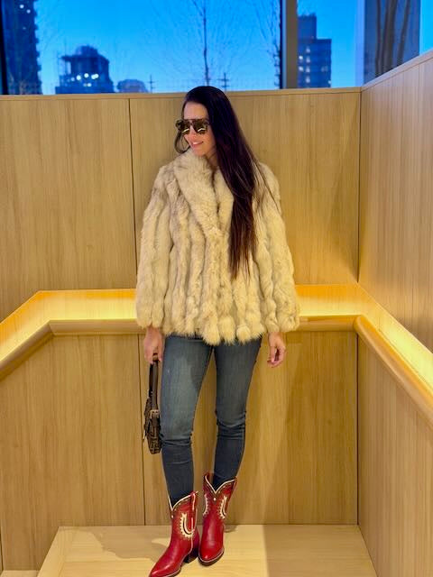 Woman wearing a fur coat, jeans, and red boots in a wooden indoor setting.