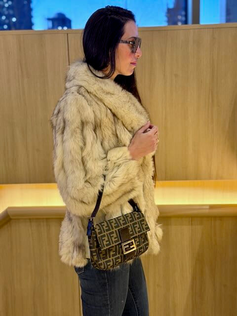 Woman wearing a fur coat and holding a patterned handbag indoors.